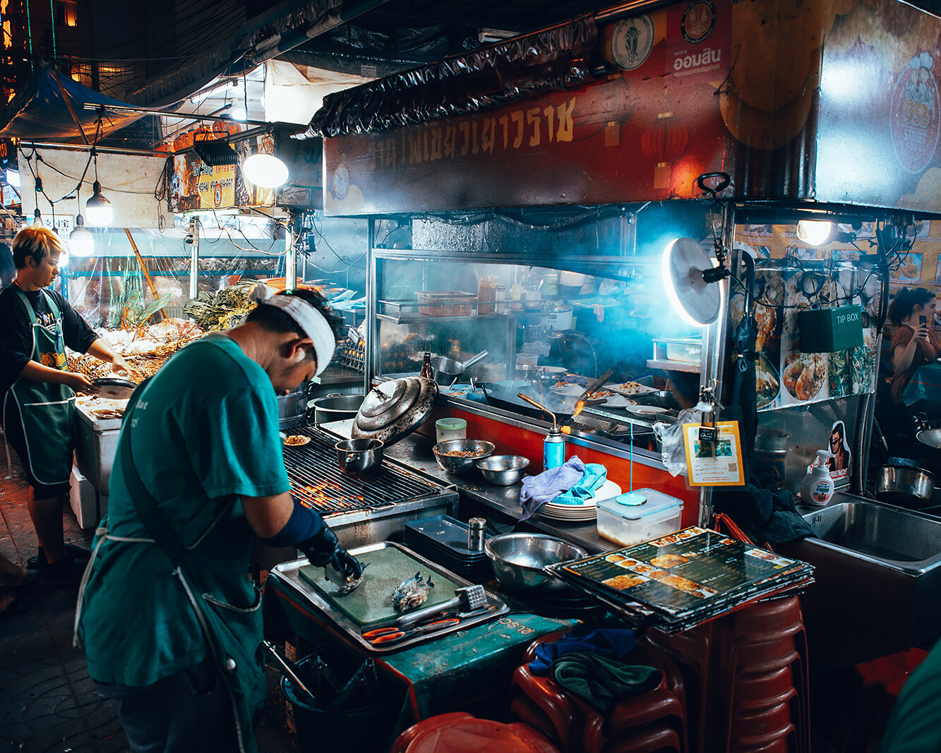 Street food cook working at a busy night market stall in Chinatown, Bangkok, Thailand.