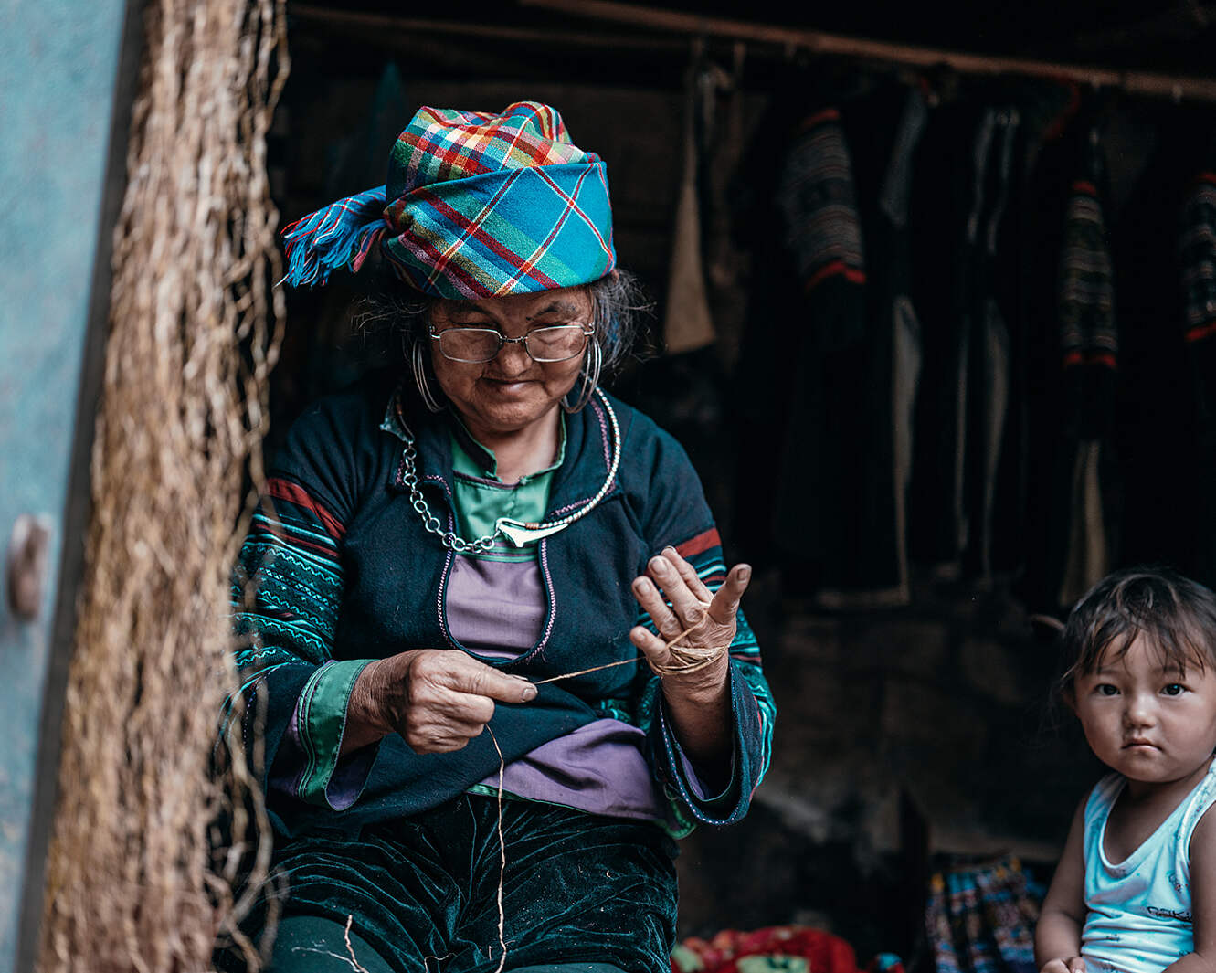 Elderly woman weaving thread inside her home while a child watches, Sapa Vietnam